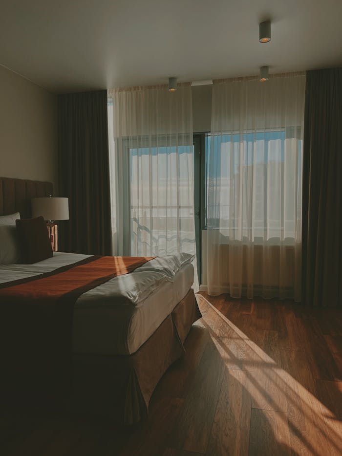 A tranquil hotel room with sunlight streaming through curtains onto a wooden floor.